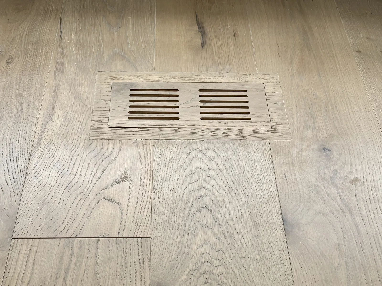 Wide-plank oak flooring mid-installation, with a floor register cut from the same board